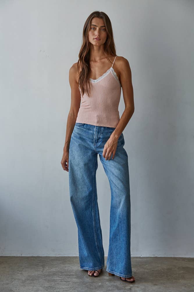 Woman in an ash rose short-sleeve top and wide-leg blue jeans stands against a light gray wall.