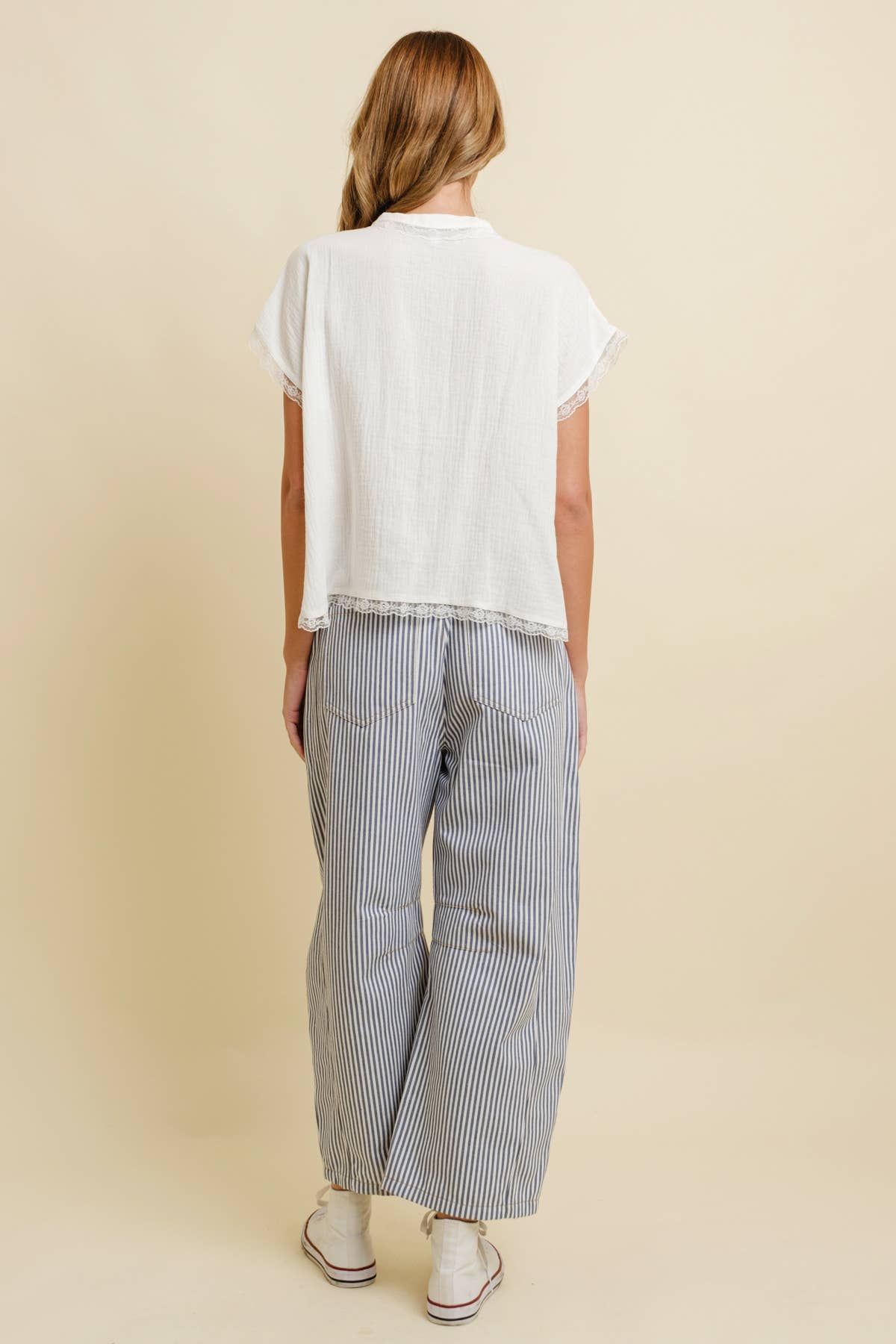 Woman wearing a white top, blue-and-white striped wide-leg pants, and white shoes shown from the back.