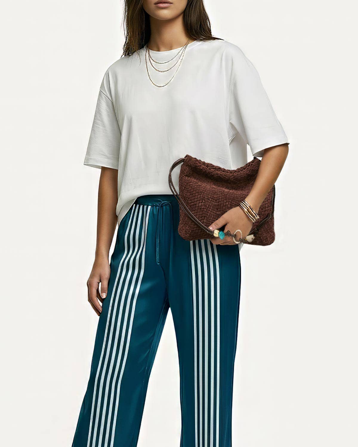 Woman in a white shirt and striped pants carrying a leather shoulder bag, styled with layered necklaces.