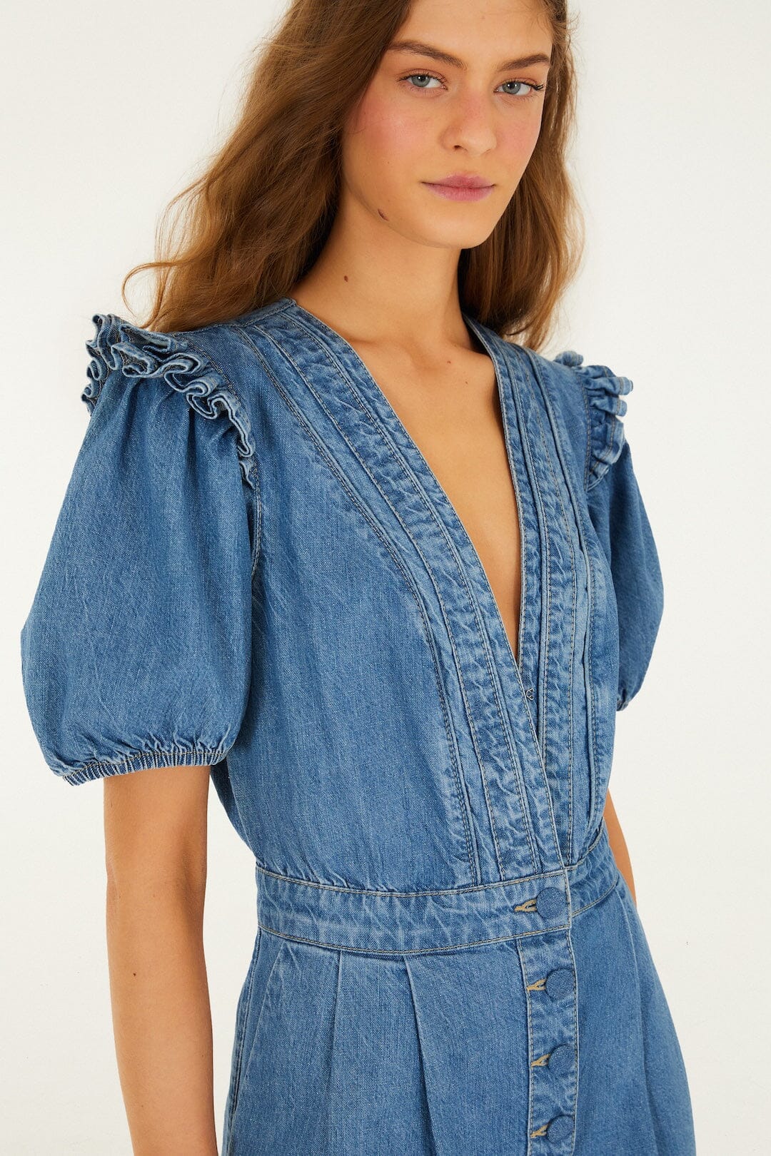Blue denim romper with puff sleeves, ruffle trim, and deep V-neck; casual wear suitable for warmer weather.
