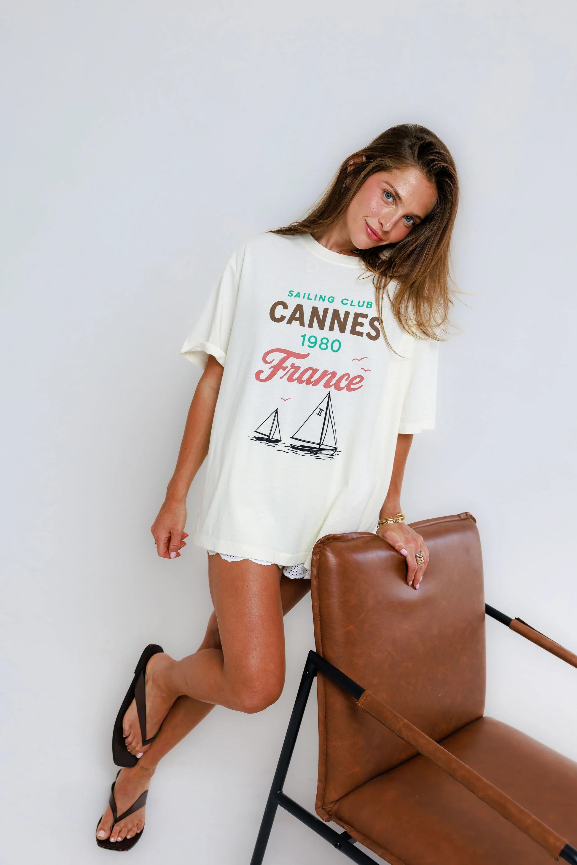 Woman in off-white cotton tee and shorts, leaning on a brown chair.