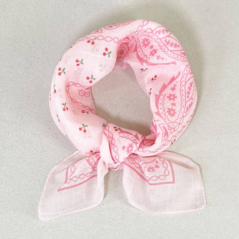 Light pink bandana with a floral paisley print and red cherries, made of soft fabric, knotted for versatile wear.