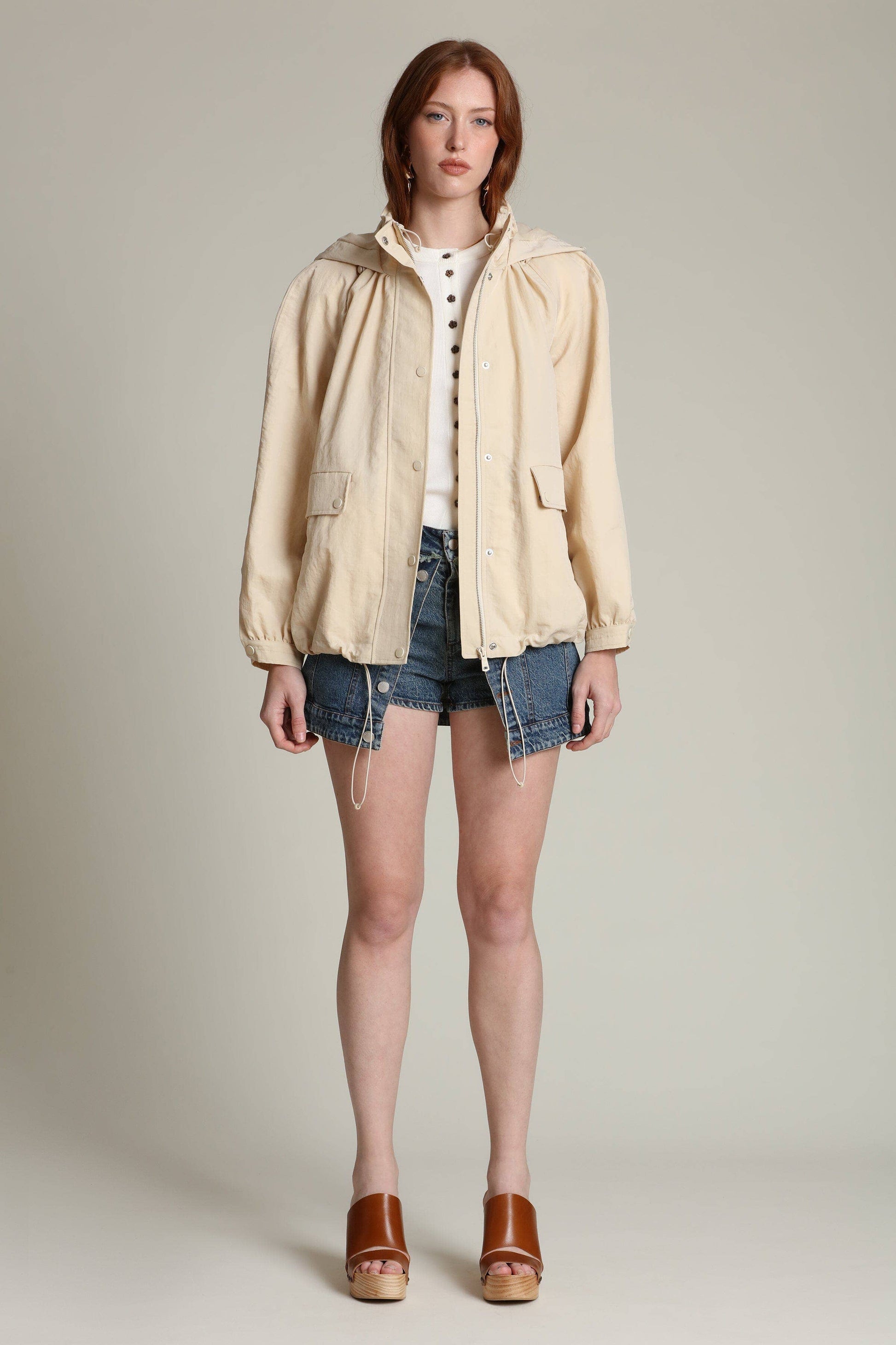 Woman wears a balloon sleeve windbreaker, white top, denim shorts, and brown sandals against a plain background.