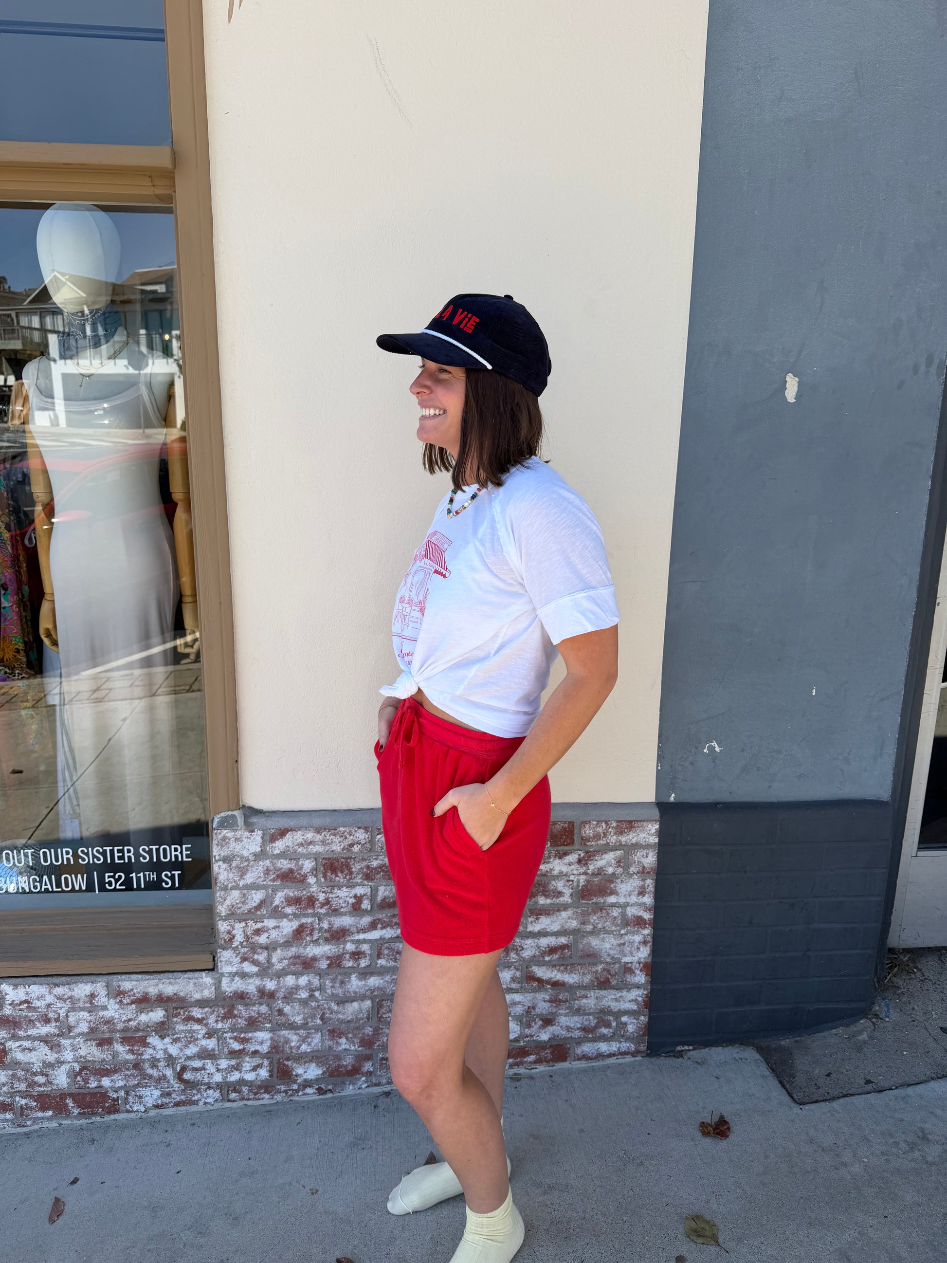 Woman wearing a white T-shirt and vermillion terry mini skirt stands outside, smiling with hands in her pockets.