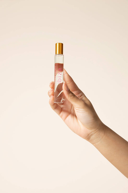 Hand holding gold-capped perfume roller on beige background, highlighting the products compact size and metallic finish.