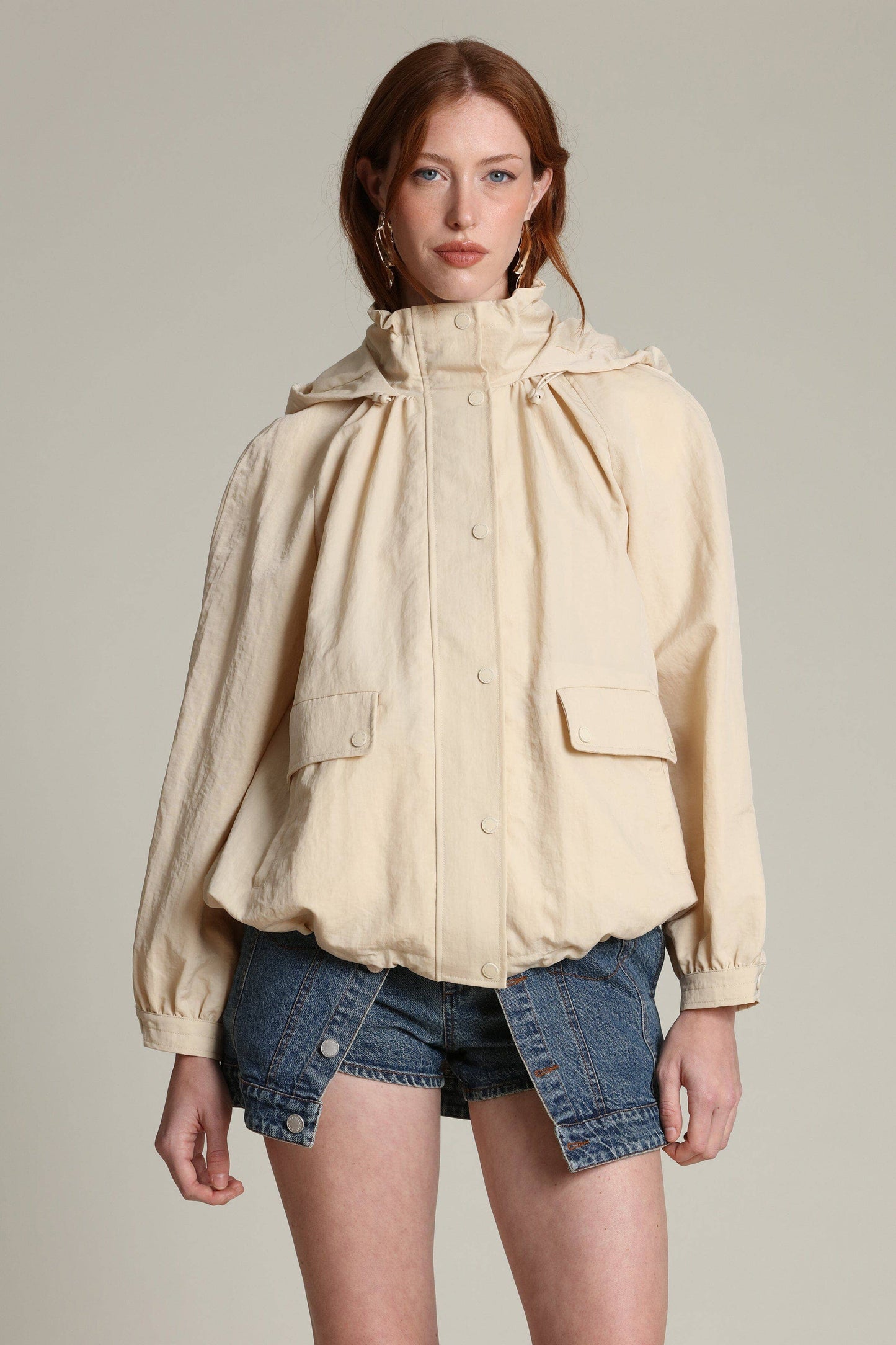 Woman in a lightweight balloon-sleeve windbreaker and blue denim shorts standing against a plain background.