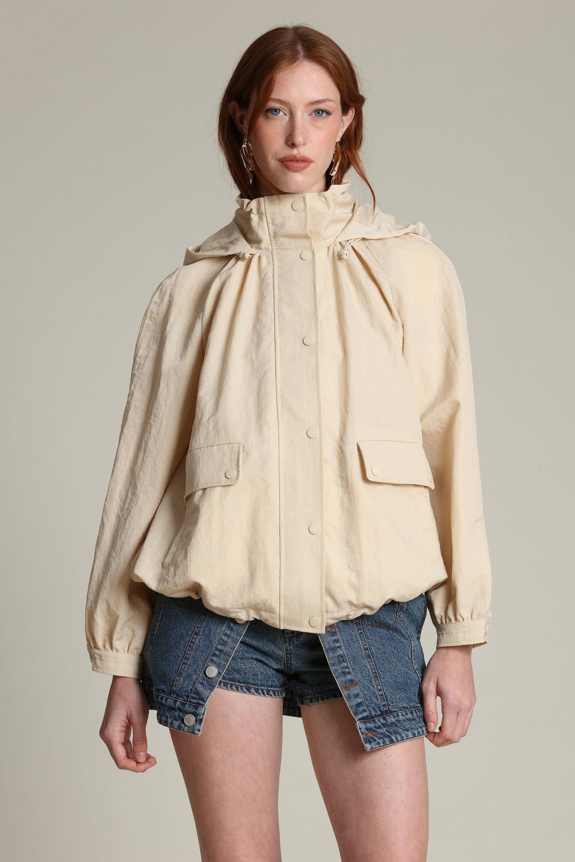 Woman in a lightweight balloon-sleeve windbreaker and blue denim shorts standing against a plain background.