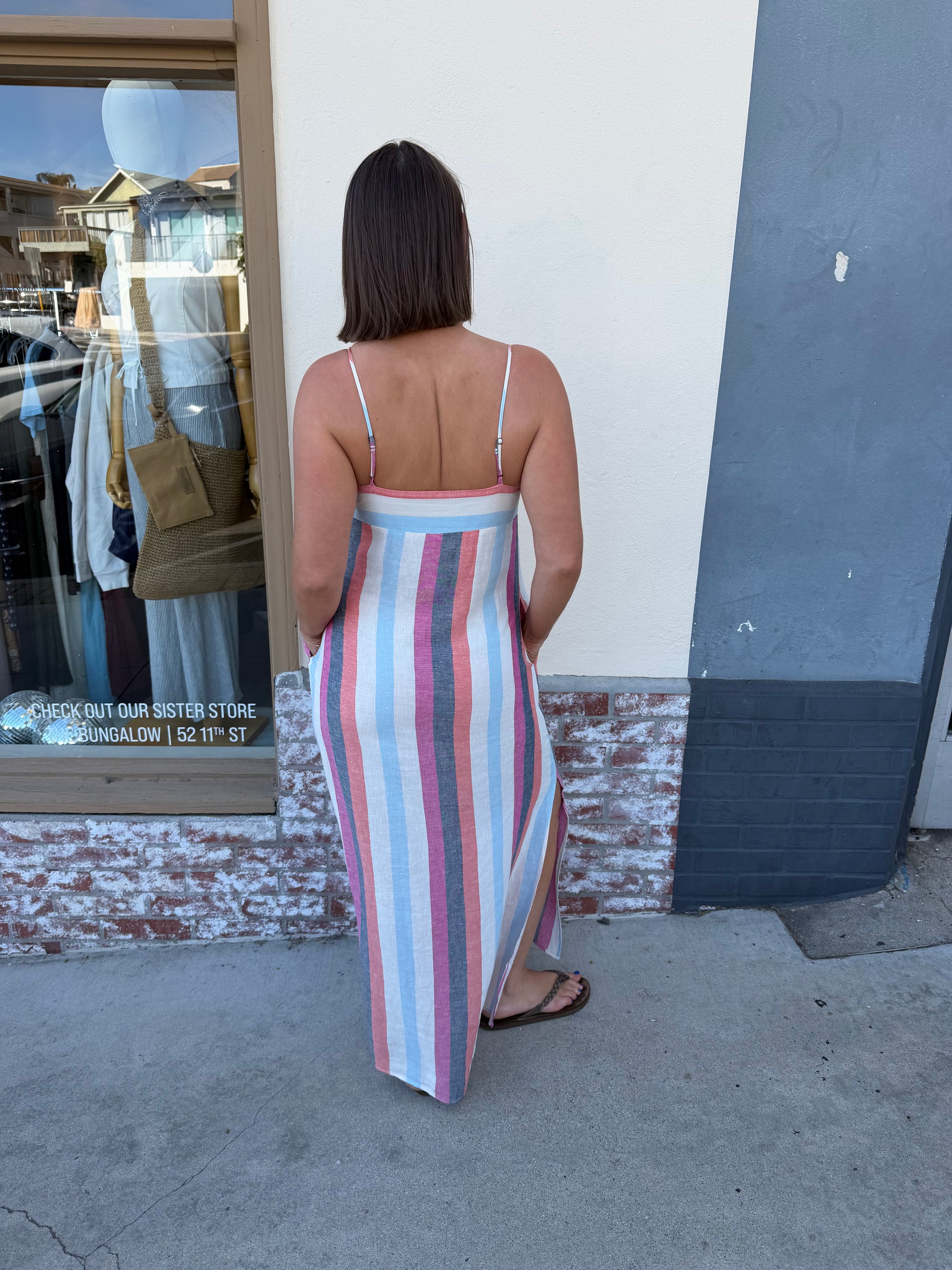 Woman wears a multi-colored striped Park Slope dress standing outside a shop on a sunny day.