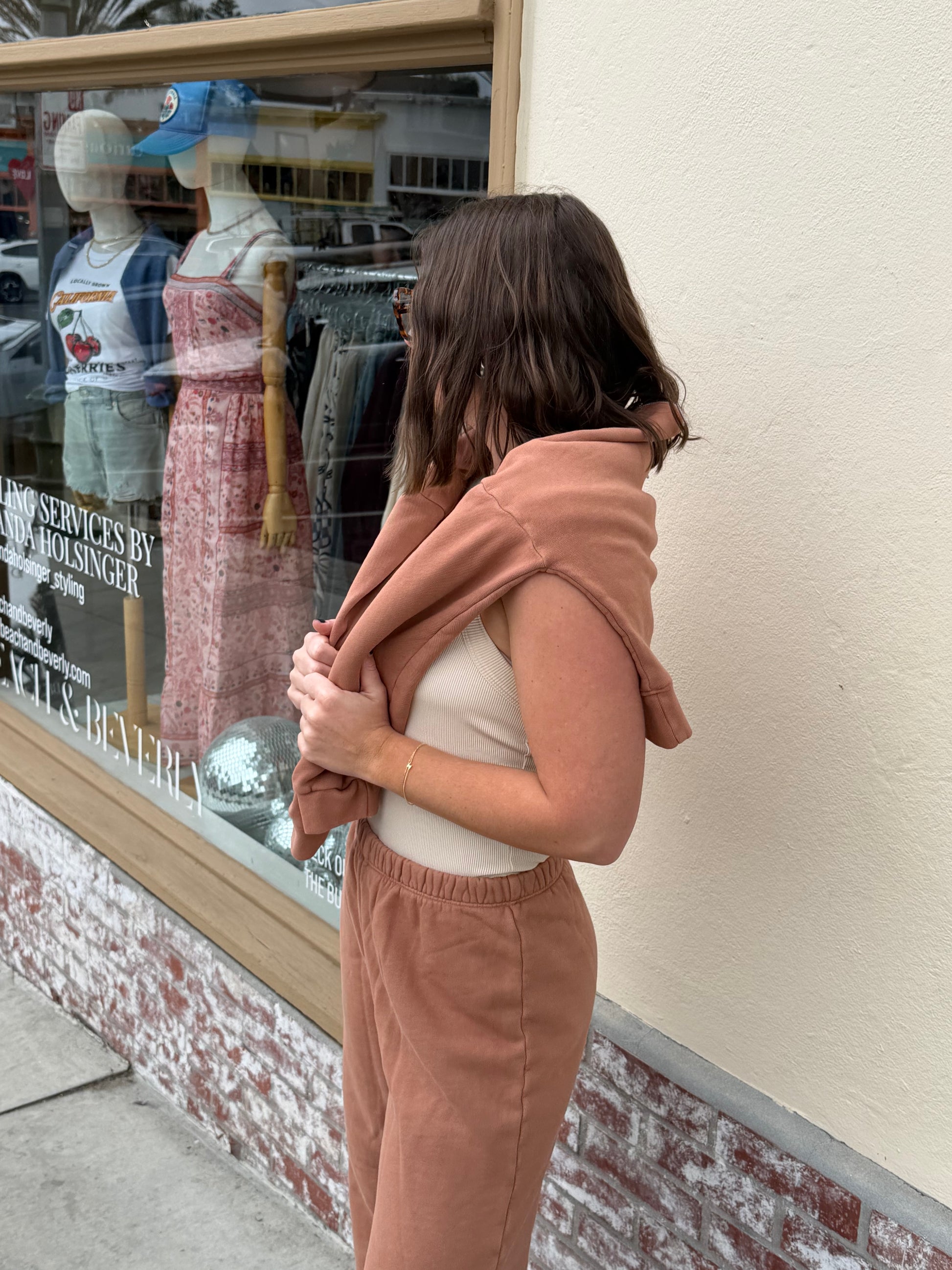 Woman outside a store wears cream wide-leg pants and drapes a sweater over her shoulders.