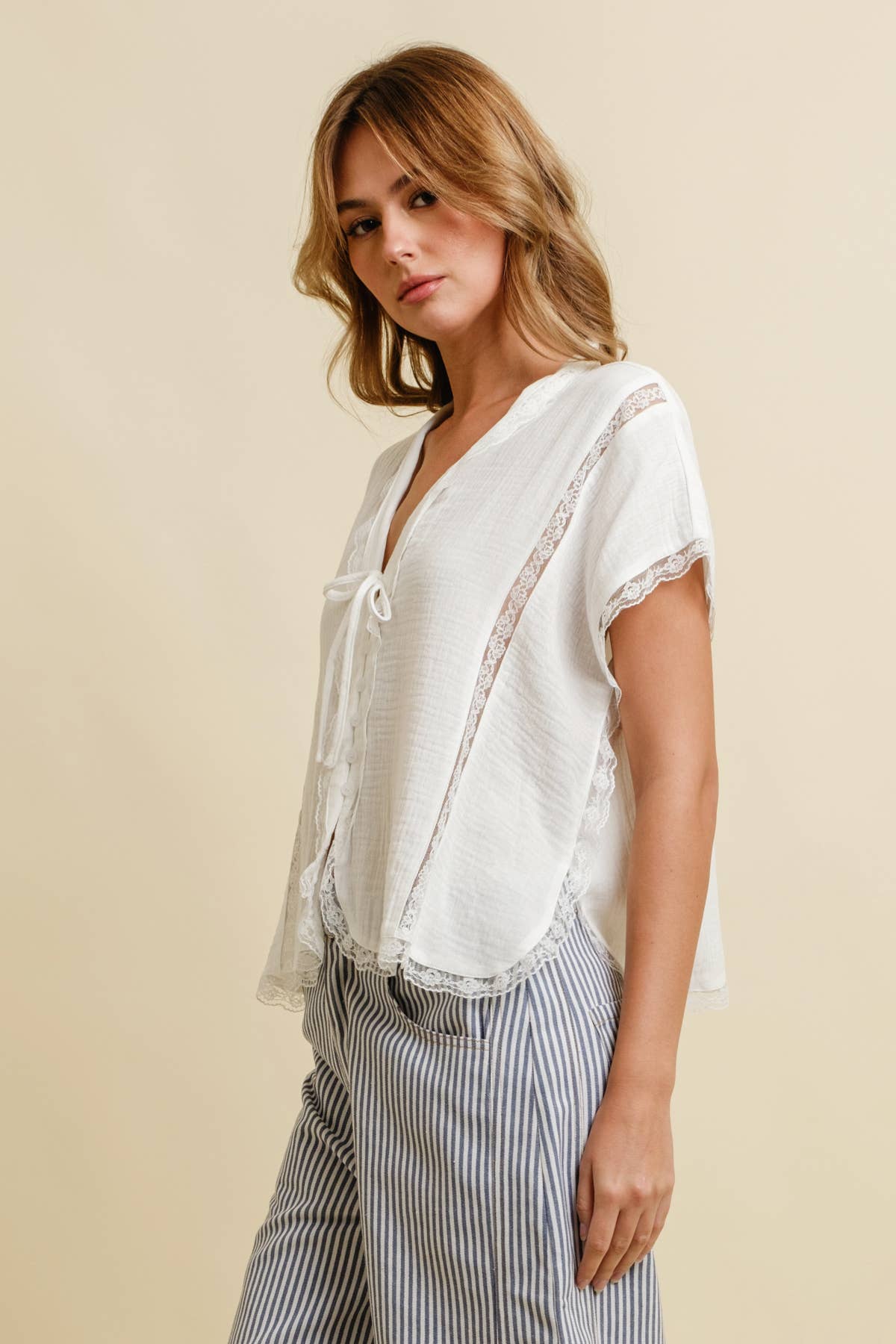 Woman wears a light knit top and black-and-white striped pants, pictured against a plain neutral background.