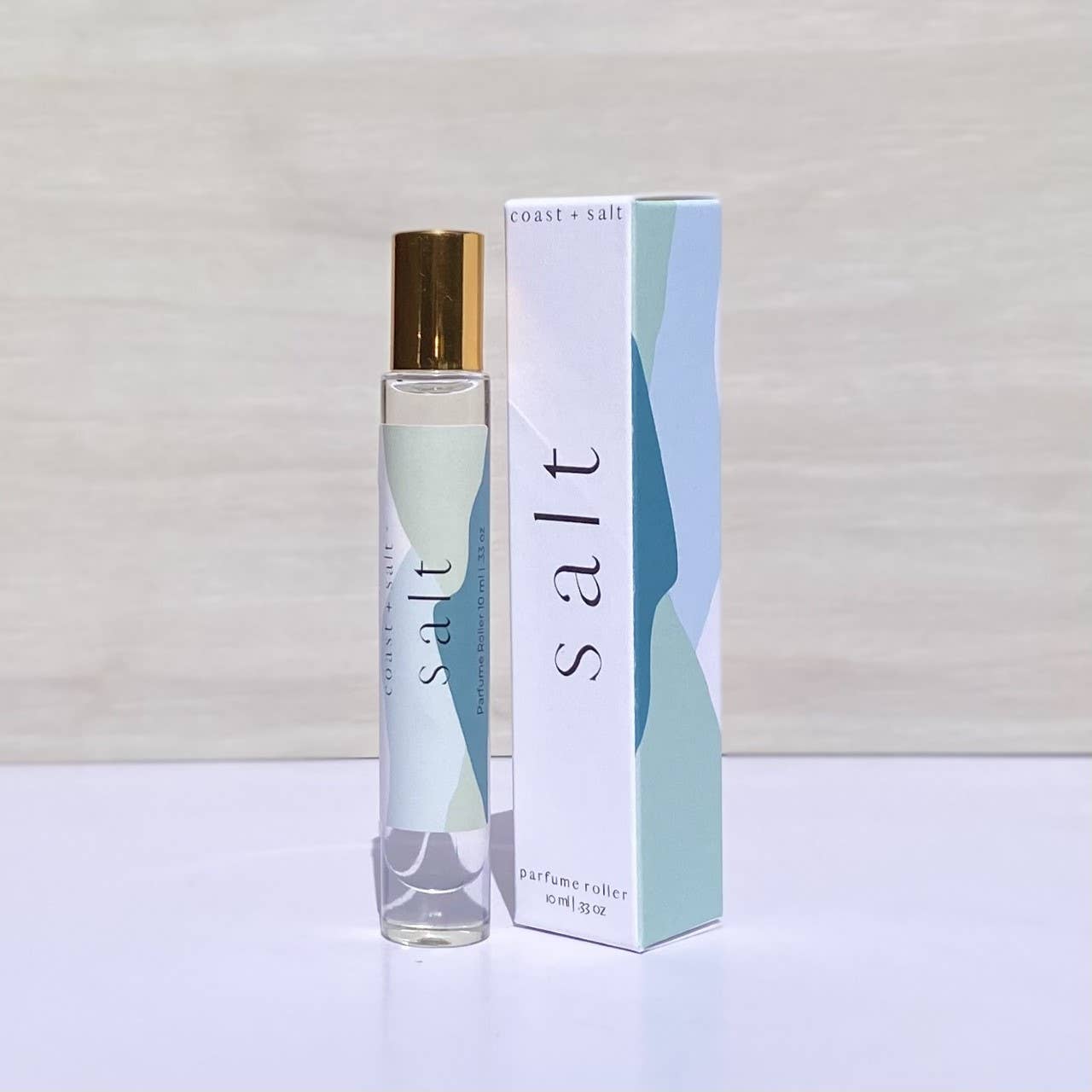 Salt perfume roller with driftwood notes beside a pastel-colored, abstract-patterned box.