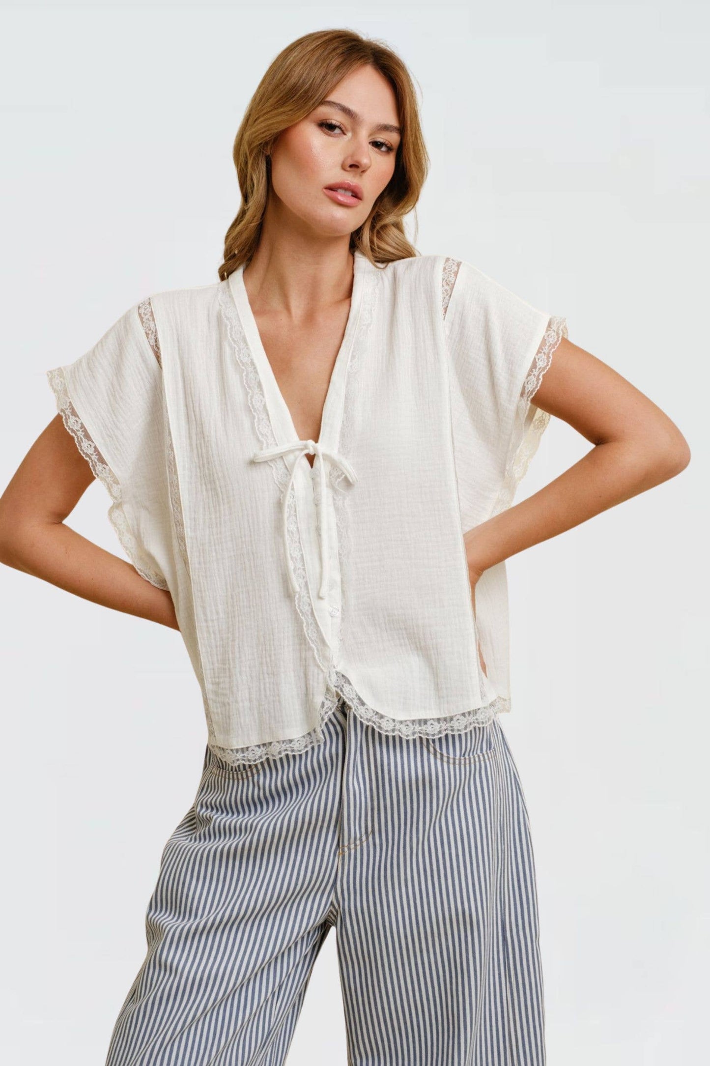 Off-white tie-front lace-trim top paired with striped wide-leg pants; woman stands with hands on hips.