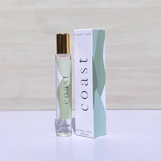 Sandalwood Coast+Salt perfume roller displayed next to its box featuring an abstract green and white design.