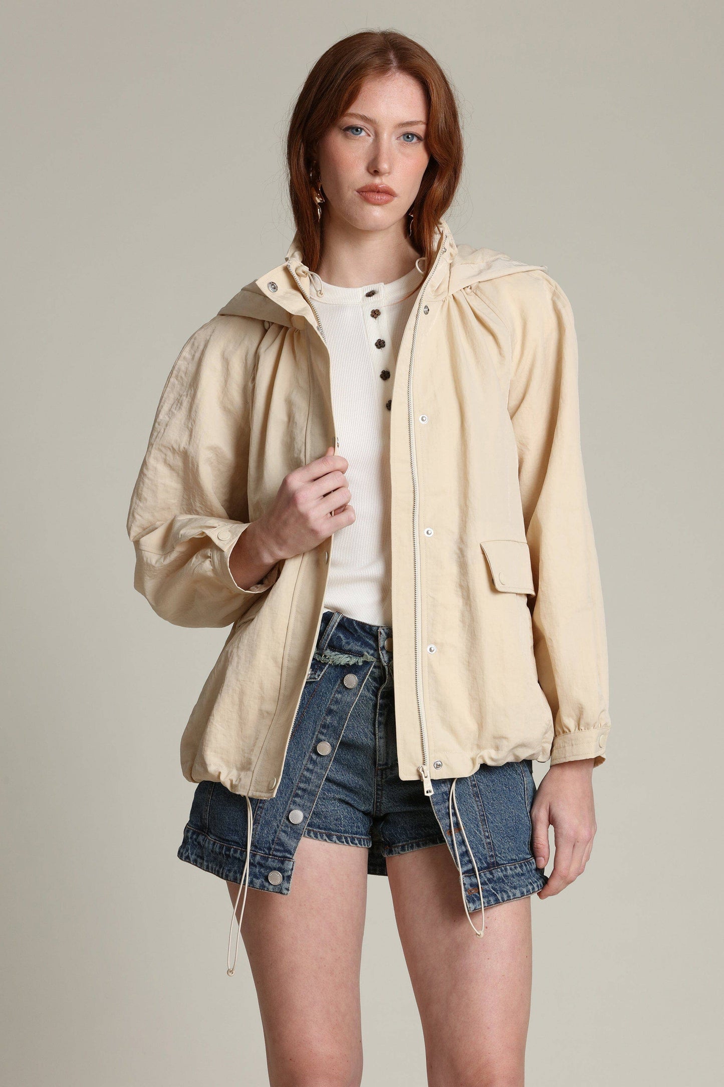 Woman in a light balloon-sleeve windbreaker, white top, and denim shorts, poses against a plain background.