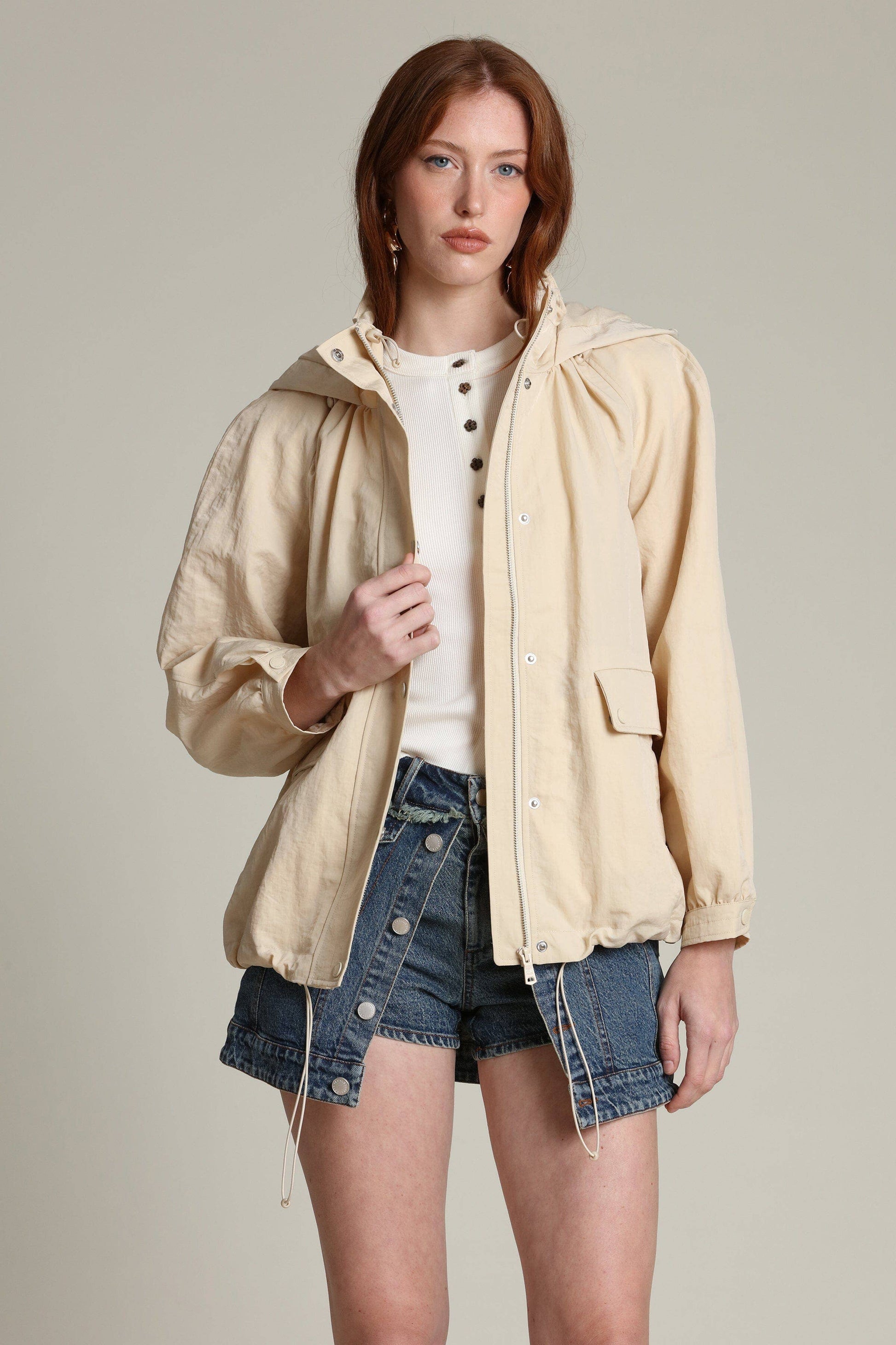 Woman in a light balloon-sleeve windbreaker, white top, and denim shorts, poses against a plain background.