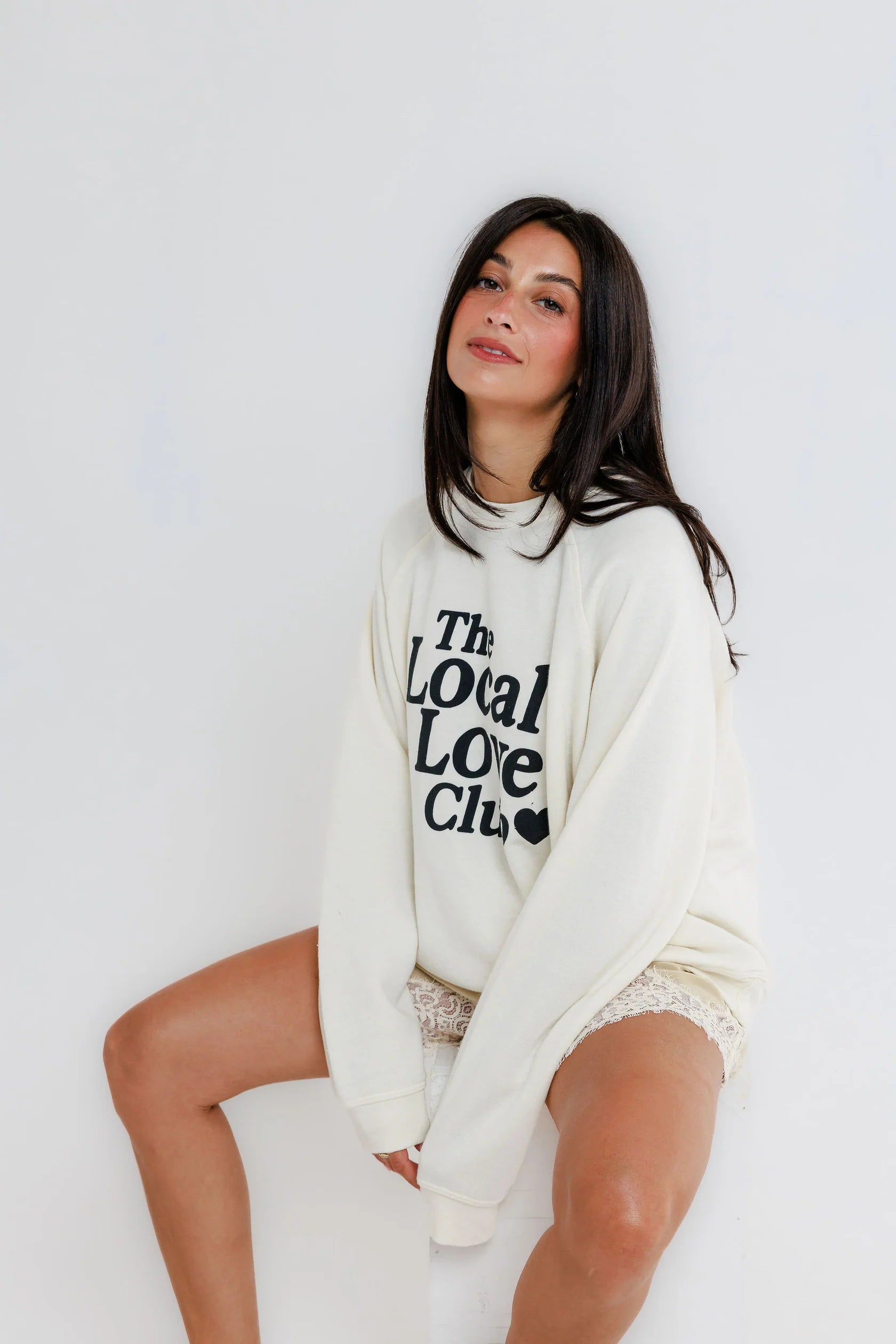 Woman wearing a yellow cotton raglan crewneck sweatshirt sits against a plain white background.