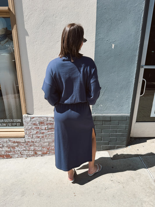 Woman wearing a navy half-zip sweatshirt stands on a sidewalk outside a store, facing away.