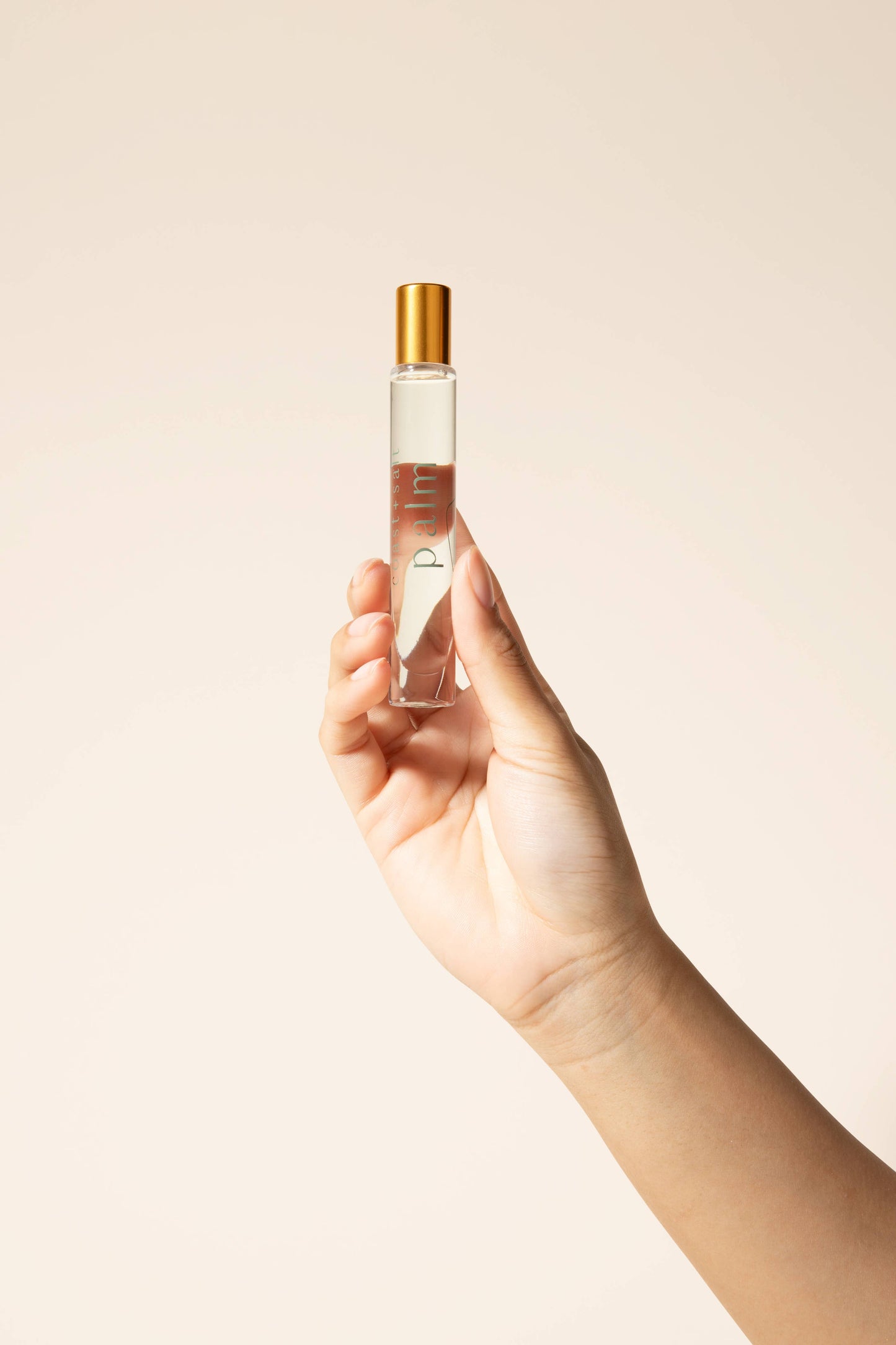 A hand holds a glass Coast+Salt Palm Perfume Roller with beach-inspired scent, suitable for easy, on-the-go fragrance use.