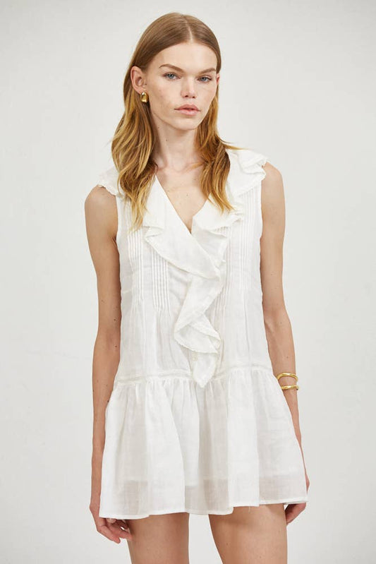 Woman in sleeveless linen mini dress with pintuck ruffle collar, paired with gold earrings and bracelet.