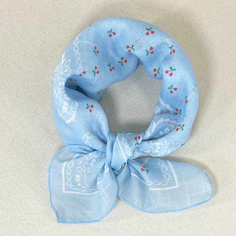 Light blue cotton bandana featuring white paisley patterns and red cherry accents, displayed on a plain background.
