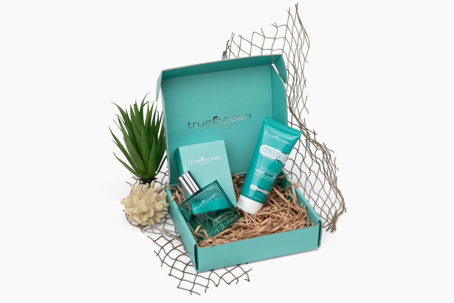 Turquoise gift box containing Mineral Lotion, ocean water body care items, mesh netting, plant, and faux coral decor.