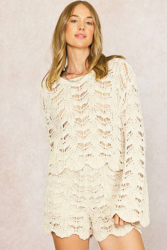 Woman wears cream crochet top and natural crochet shorts, standing against a plain light-colored background.