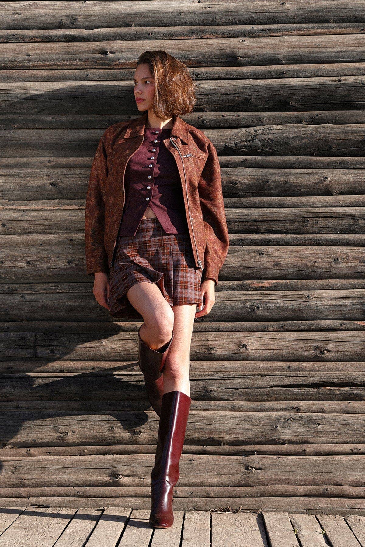 Woman wearing a floral print bomber jacket, cotton blend, stands by a wooden wall, looking to the side.