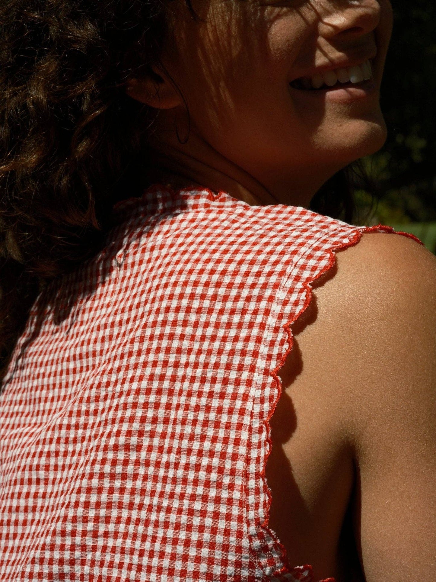 Person in sunlight wearing a red and white gingham cotton sleeveless square-neck top.