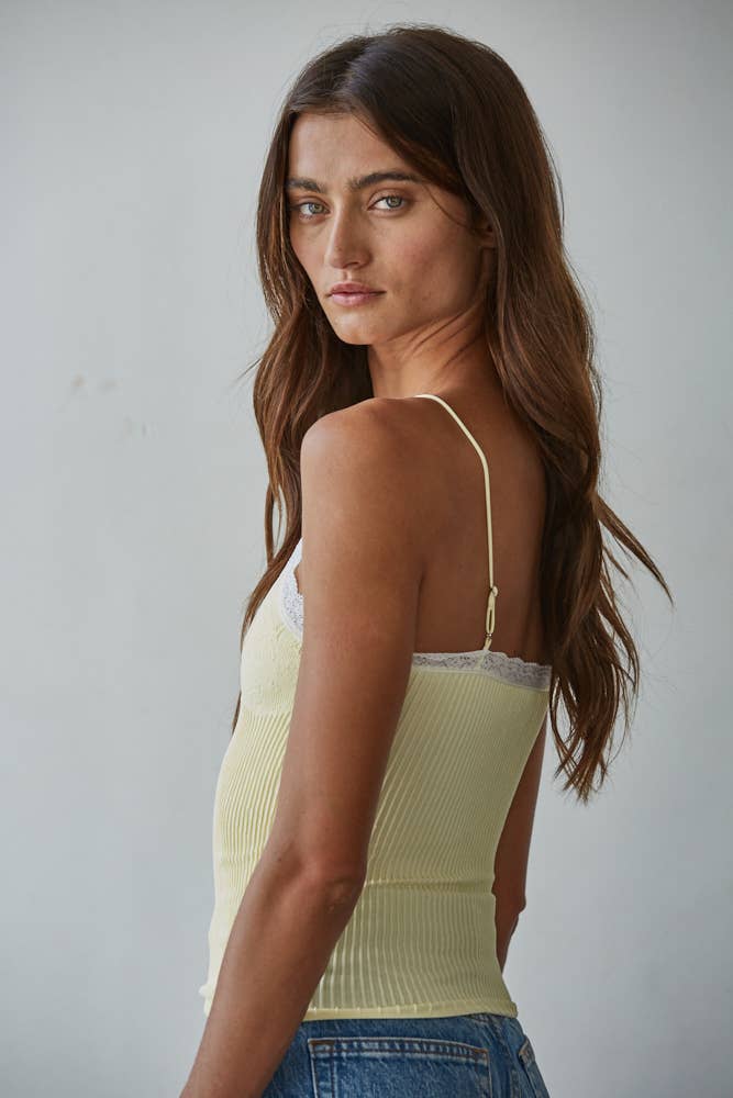 Woman with long brown hair in a yellow lace v-neck camisole and blue jeans.