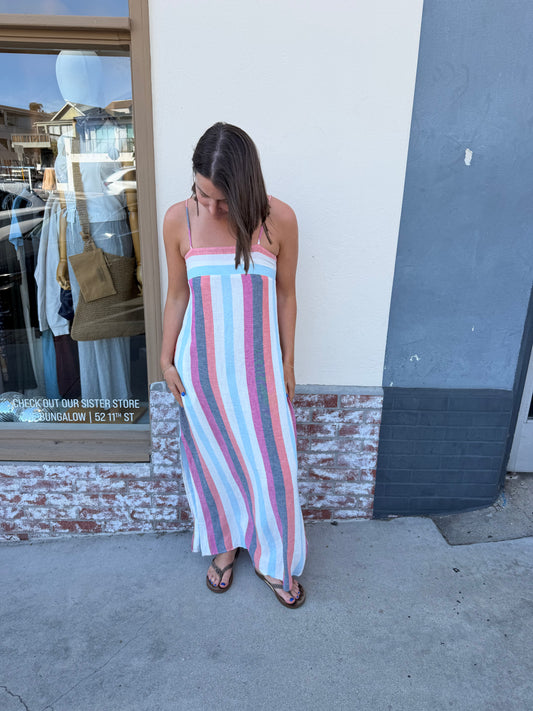 Woman wearing a striped multi-color midi dress with pockets stands on the sidewalk. Cotton-blend fabric, casual use.