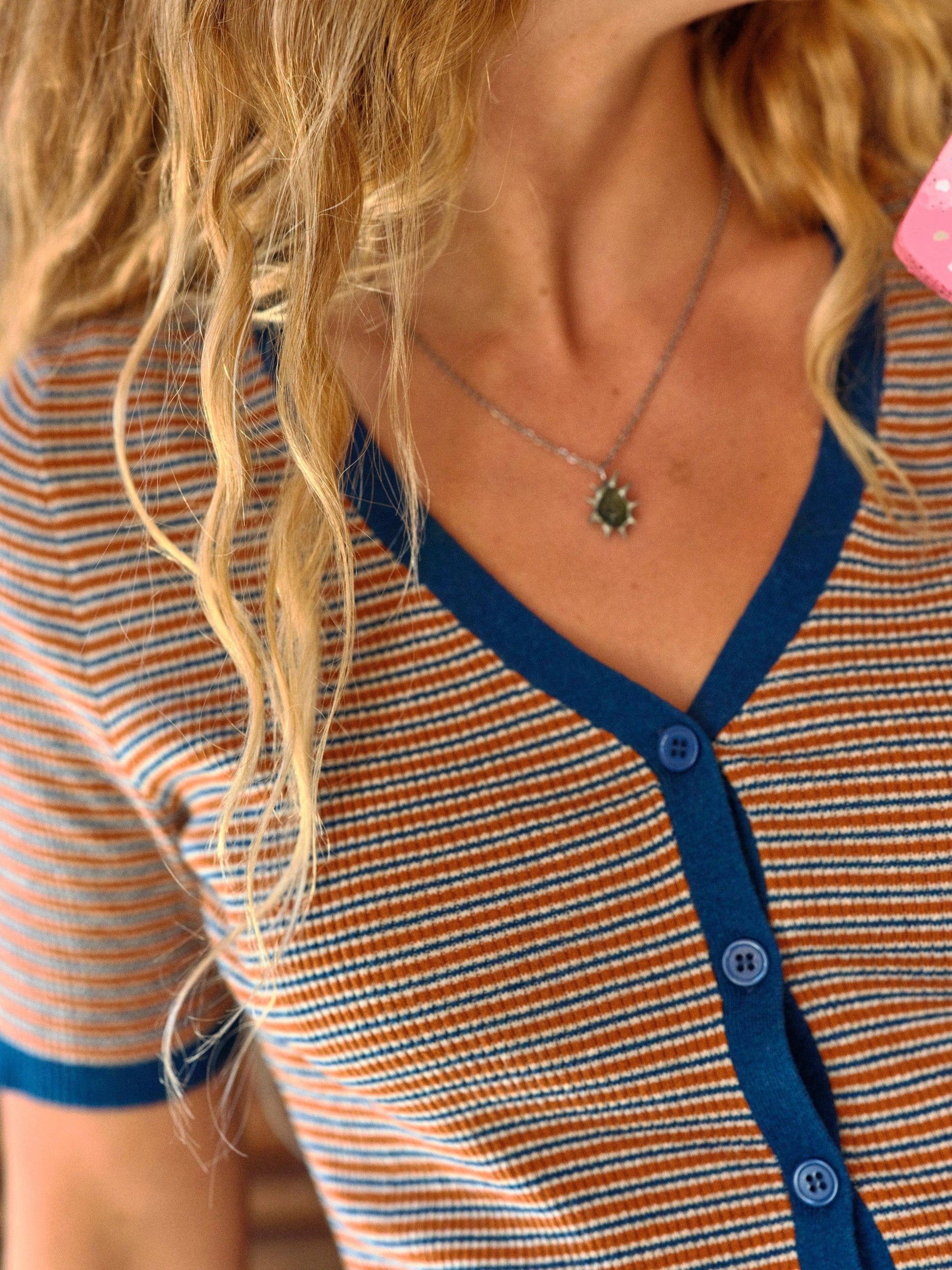 Person with wavy blonde hair in a light cotton tee and pendant necklace.