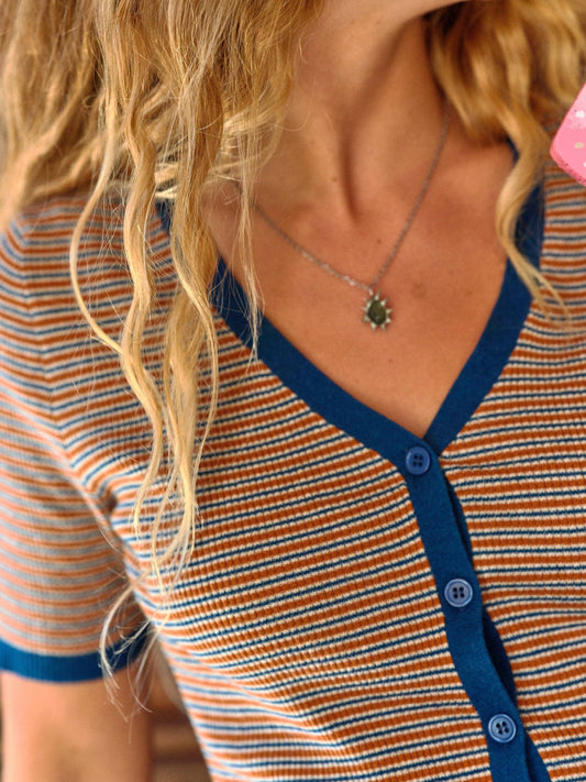 Person with wavy blonde hair in a light cotton tee and pendant necklace.