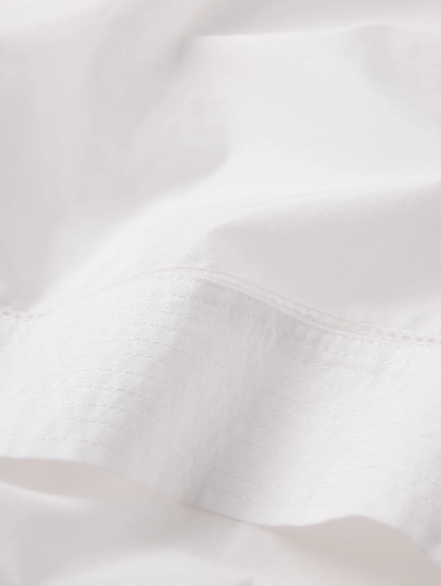 White silk cape shirt with visible stitching and a subtle textured pattern, shown in close-up for fabric detail.