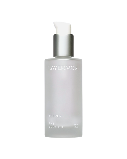 Clear frosted glass bottle of body oil with a silver pump and simple white text, meant for skin hydration.