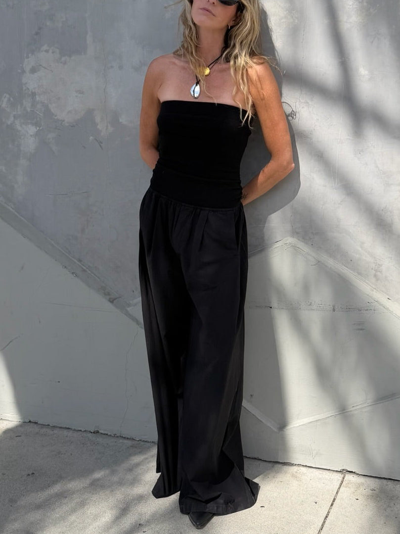 Woman in black jumpsuit and sunglasses stands against a gray wall. Jumpsuit is lightweight and suitable for casual wear.