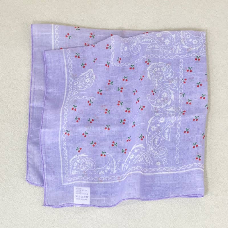 Purple bandana with white paisley and red cherry patterns, made of fabric for versatile accessory use.
