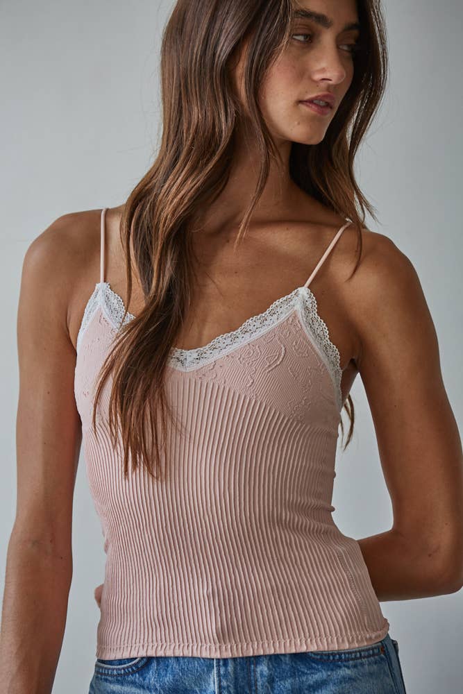 Woman with long brown hair models an ash rose knit top and blue jeans, shown in a side-facing pose.