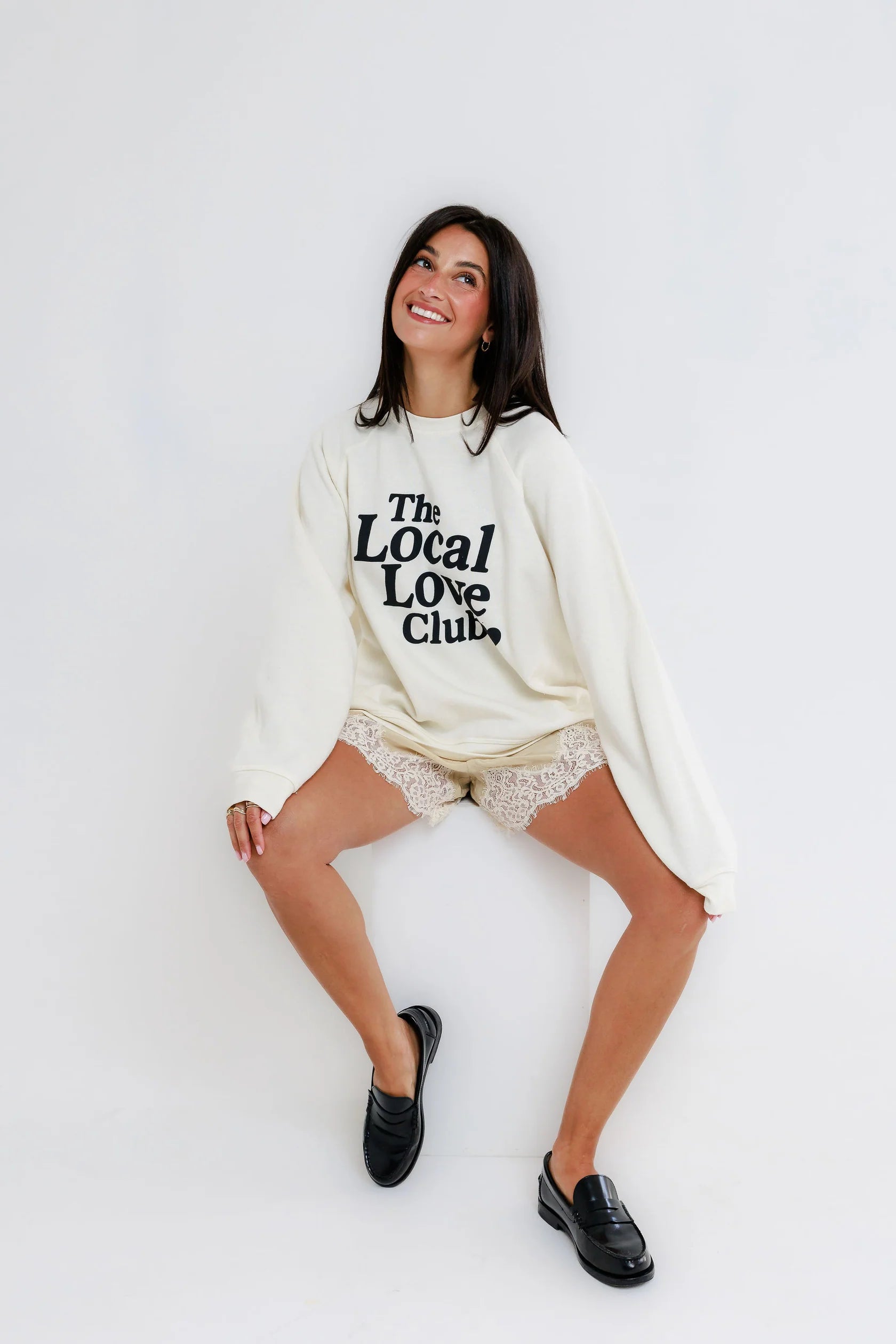 Woman wearing a cream-colored crewneck sweatshirt, lace shorts, and black loafers.