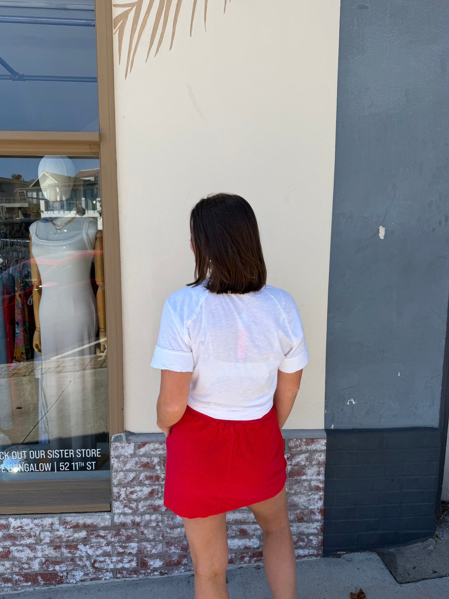 Woman in white shirt and vermillion terry mini skirt looks at shop window displays.