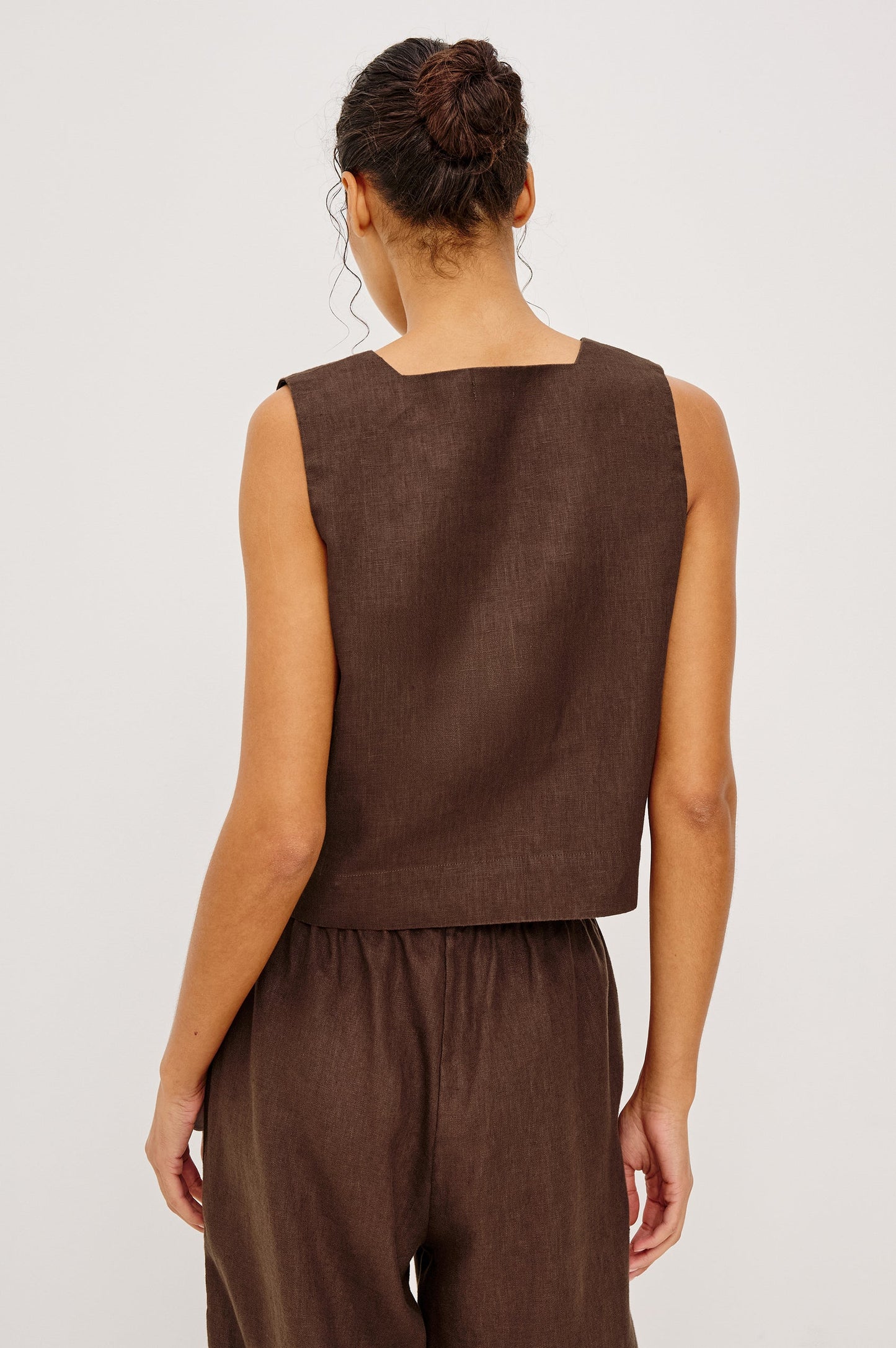 Woman models espresso-colored button-up shirt and matching pants, shown from the back against a plain background.