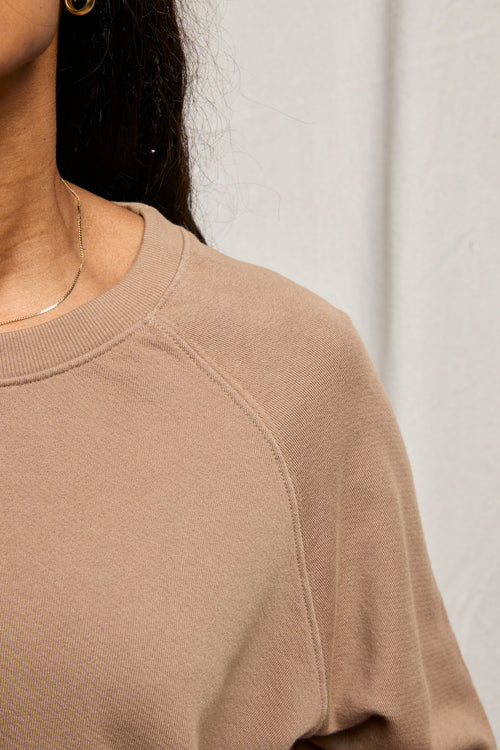 Person wearing a white cotton sweatshirt, thin gold necklace, and small gold hoop earring.