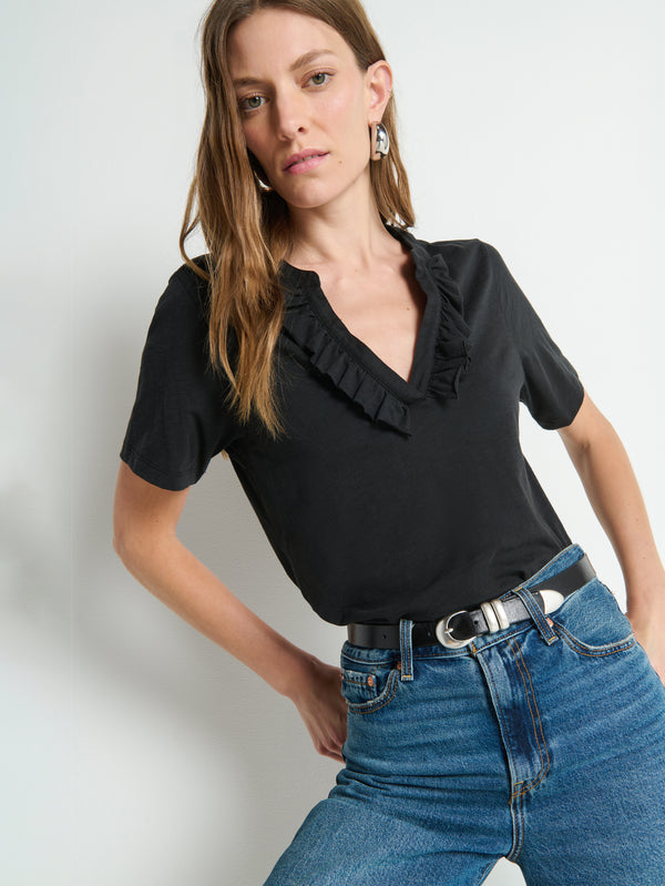 Woman wears a black short-sleeve top and blue denim jeans, standing against a plain white wall.