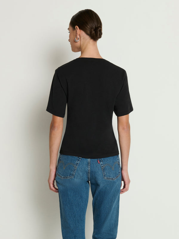 Person with short hair models a black cotton long-sleeve top and blue jeans, back view, against a light background.