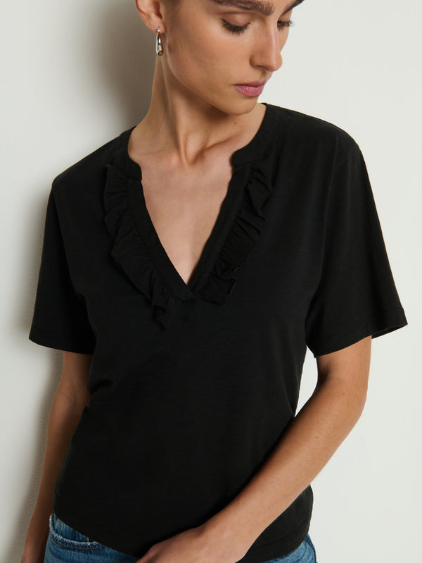 Jet black top with ruffled neckline, cotton material, worn by woman looking down in front of a light-colored wall.