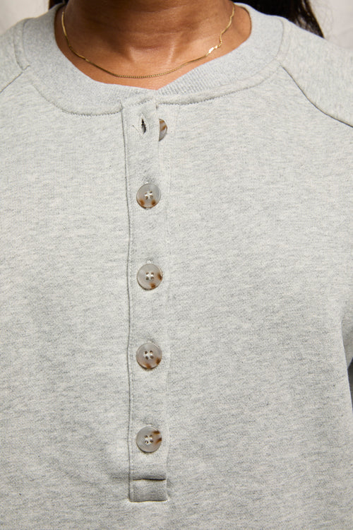 Person wearing a medium heather grey sweatshirt and a thin gold necklace, shown in a close-up view.