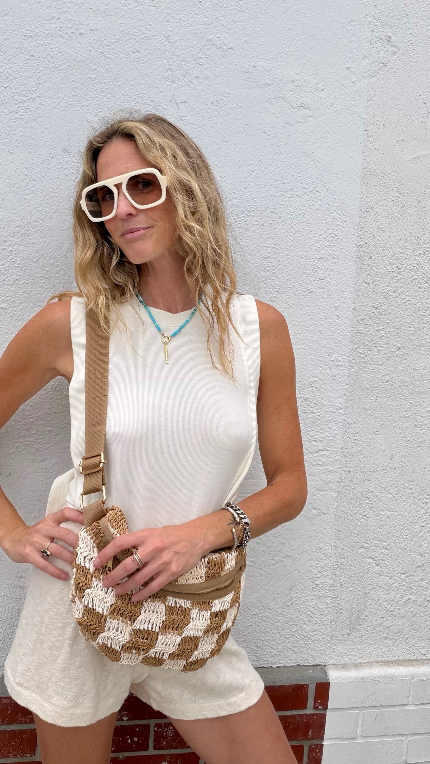 Woman in a parchment Mason open-side top, Caydn sunglasses, holding a woven crossbody bag.