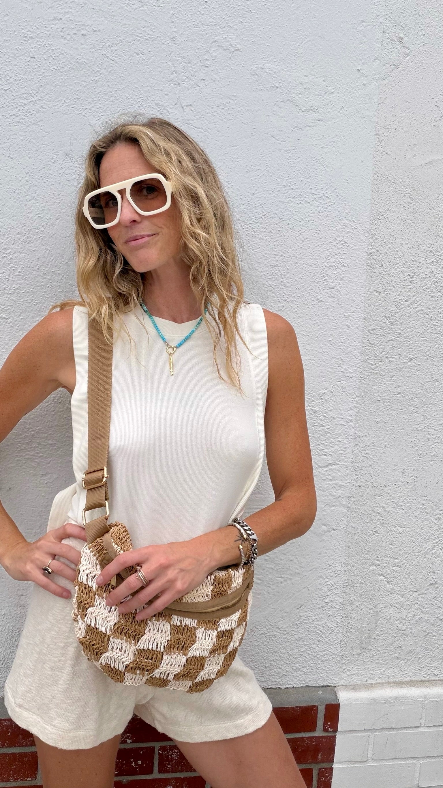 Woman in a parchment Mason open-side top, Caydn sunglasses, holding a woven crossbody bag.