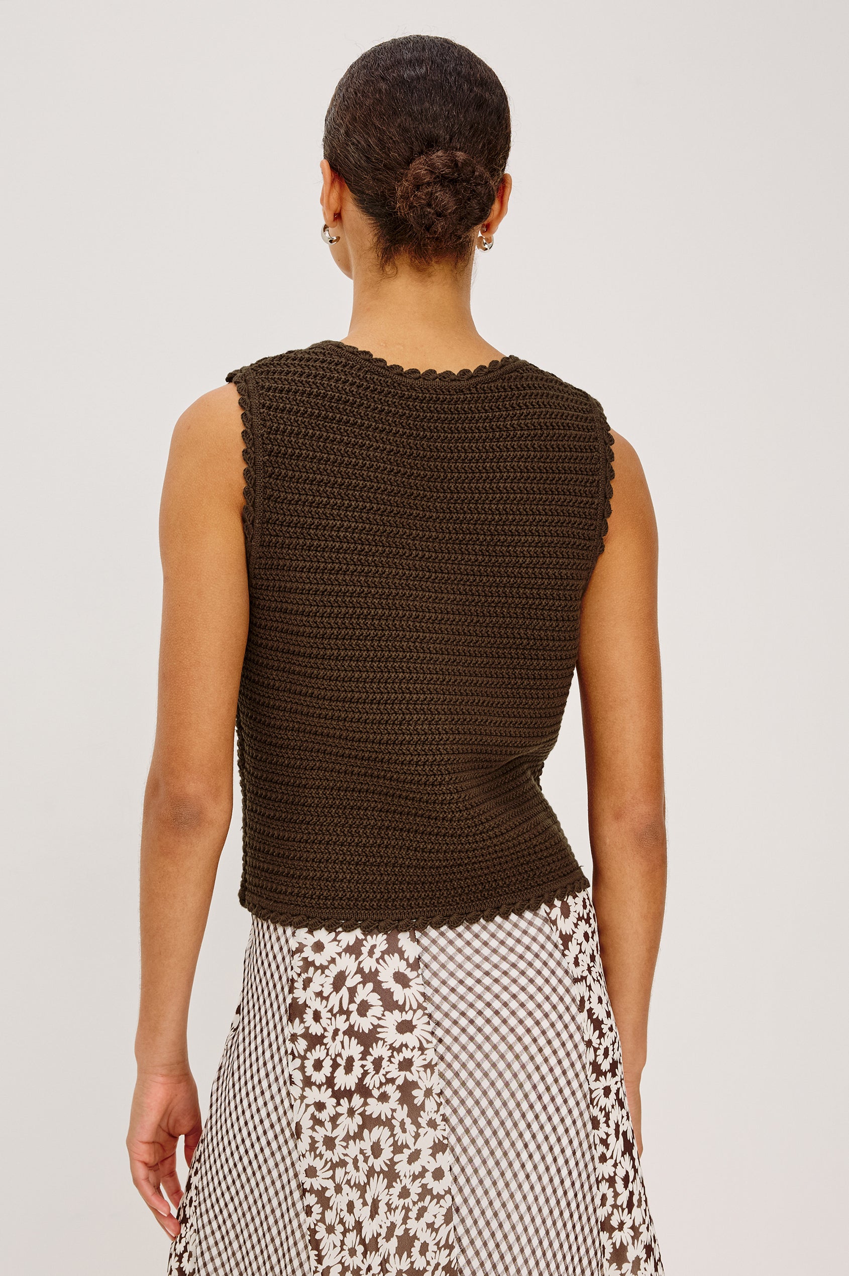 Woman with a bun, seen from behind, wears a brown vest and a floral checkered skirt.