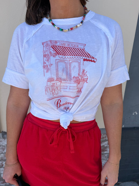 Woman in white cotton boyfriend tee, red skirt, and beaded necklace, standing outdoors.