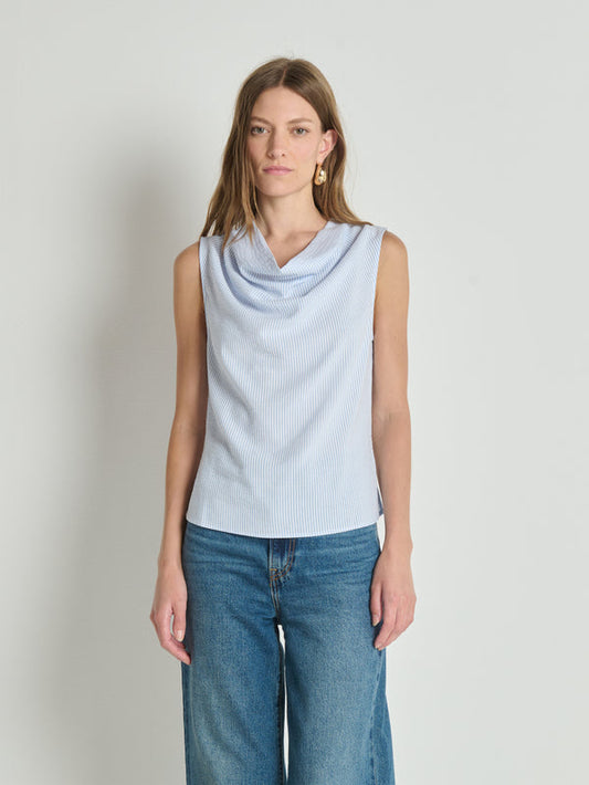 Woman in a sleeveless, striped cowl-neck tank top with blue jeans, standing against a light background.